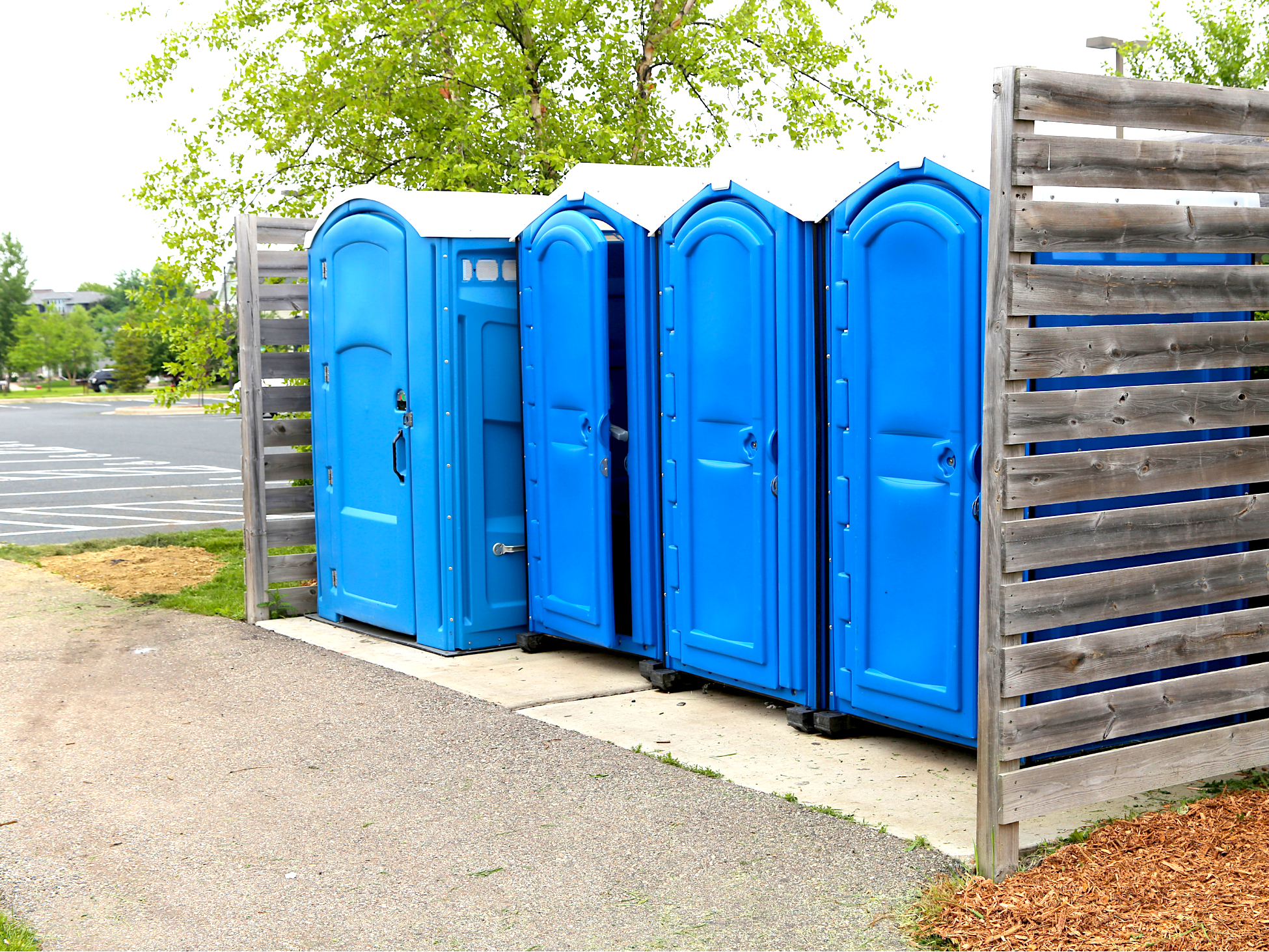 Portable restrooms inside a wooden screen enclosure beside a public park lot
